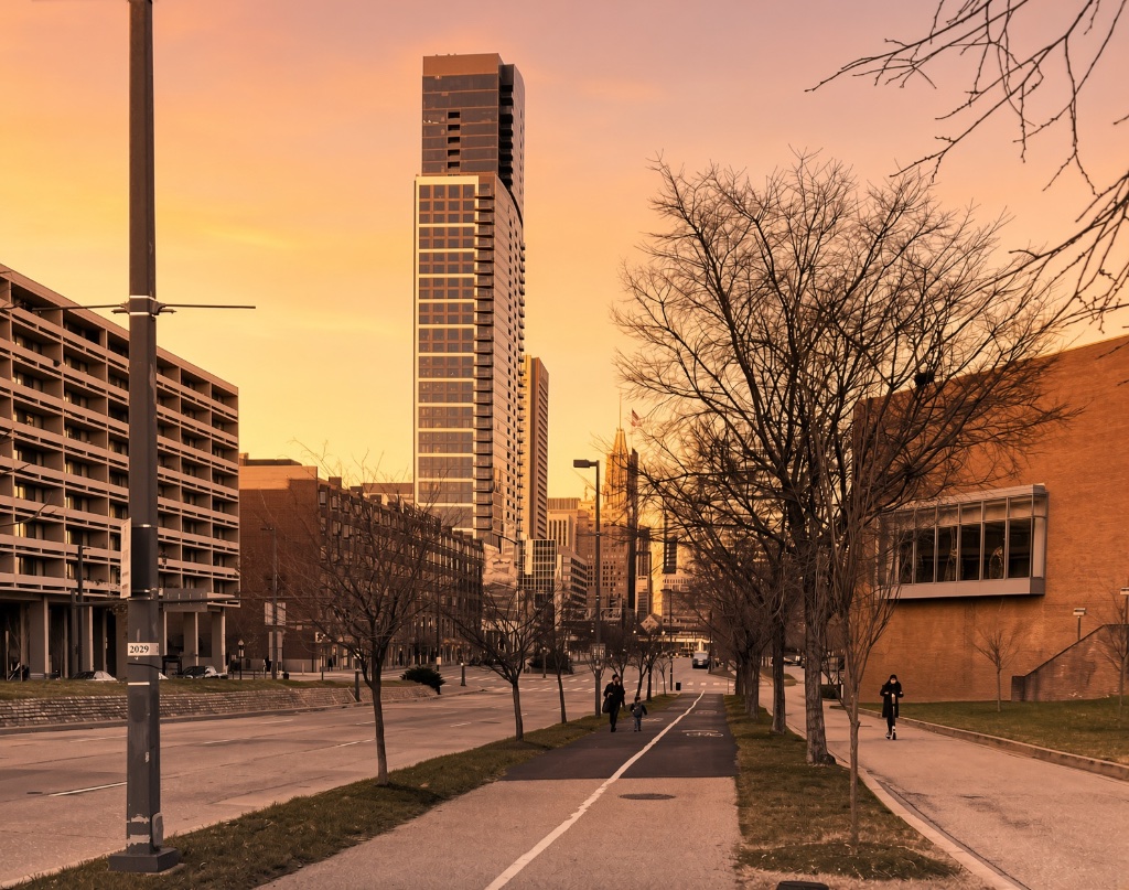 The City of Baltimore skyline at golden sunset — a downtown tower silhouetted against a warm orange evening sky