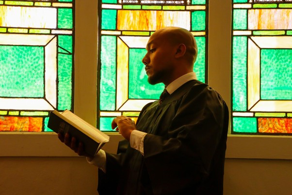 Behind the scenes - man reading book before stained glass window