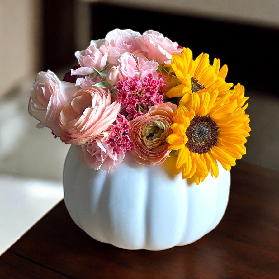 standard: Handcrafted fall sunflower bouquet in a white pumpkin-shaped ceramic vase with blush pink ranunculus and magenta waxflower for autumn flower delivery in Las Vegas NV