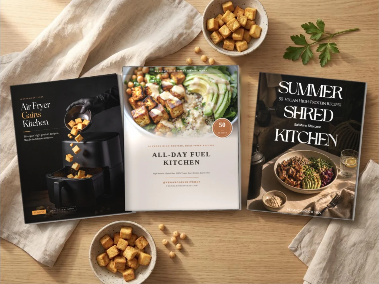 Three vegan high-protein cookbooks as printed paperbacks on a wooden table