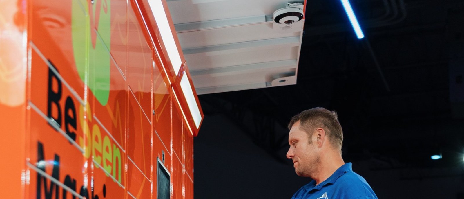 A BeSeen team member standing beside the orange BeSeen Machine lockers
