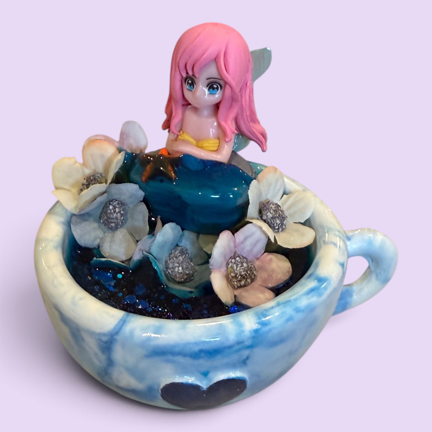Heart-Cup Daydream Mermaid - mermaid figurine with pink hair and silver tail resting in a blue marbled heart teacup with pastel blossoms and glitter