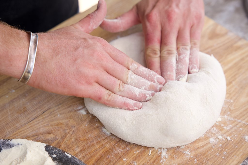 Hands pressing dough on floured board