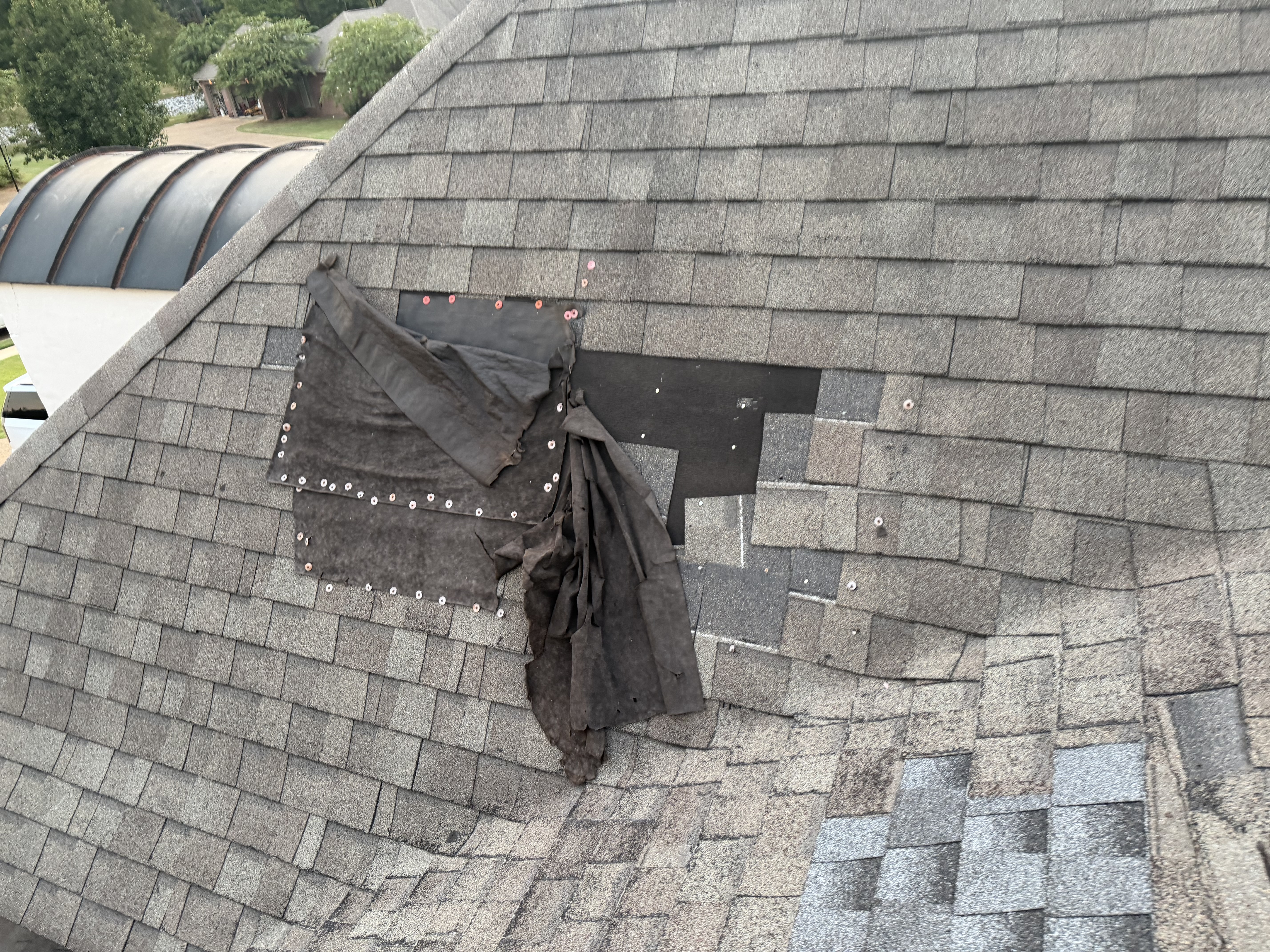 Failed roof patch with exposed underlayment and fasteners