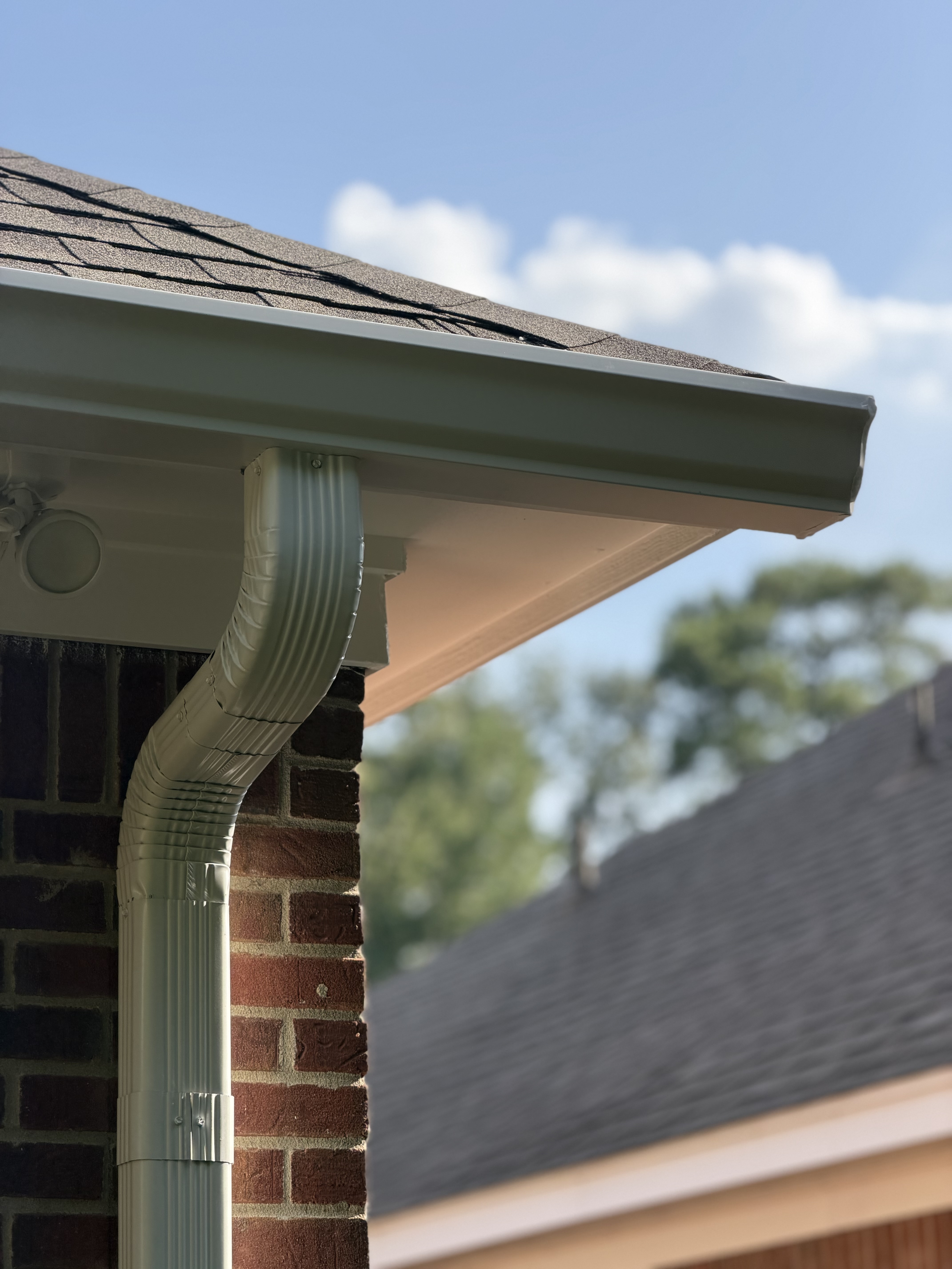 New white gutter and downspout at a brick corner