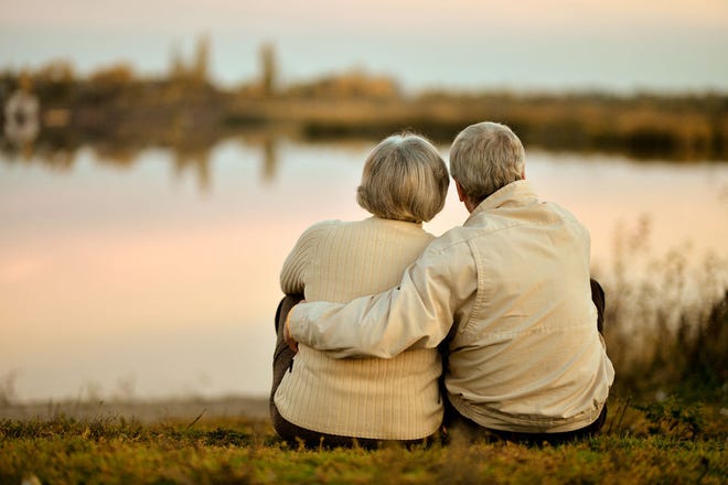 Senior couple sitting together by the lake at sunset
