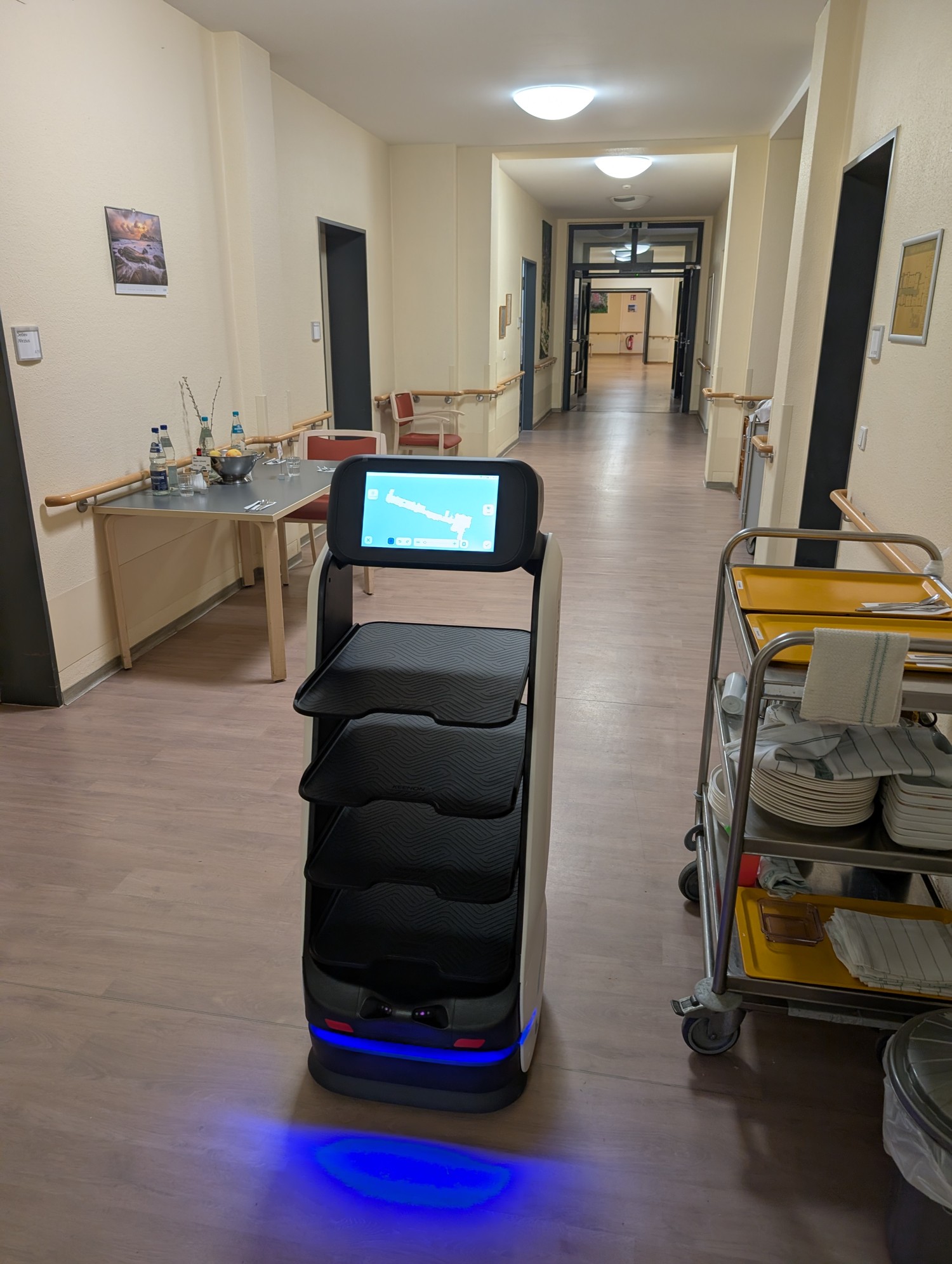 KEENON DINERBOT T9 Service-Roboter mit mehreren Ablagen im Flur der MediTerra-Einrichtung in Braunschweig neben einem Geschirrwagen