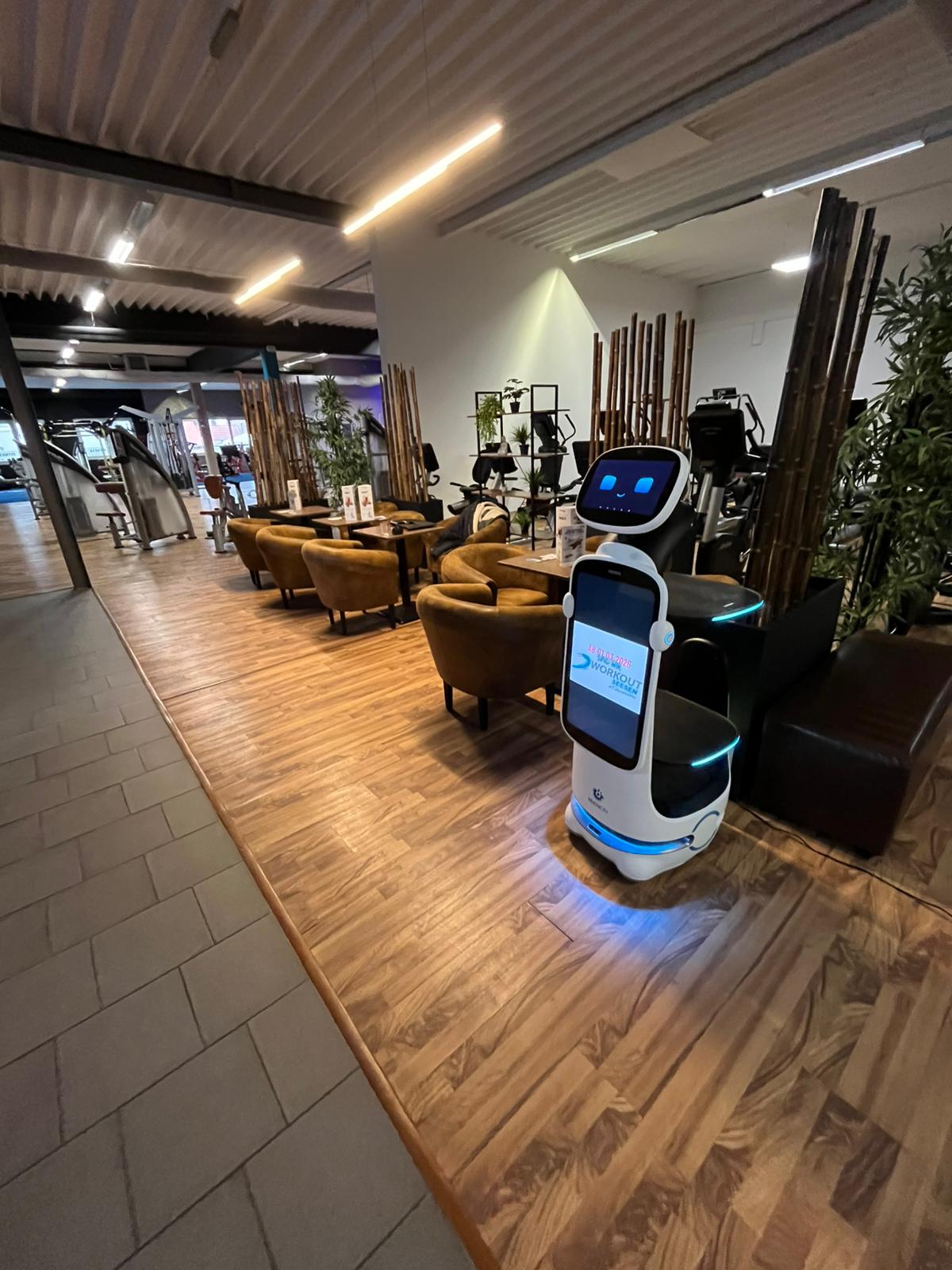Roboter mit blau beleuchteten Ablagen neben dem Lounge-Bereich im Workout Seesen