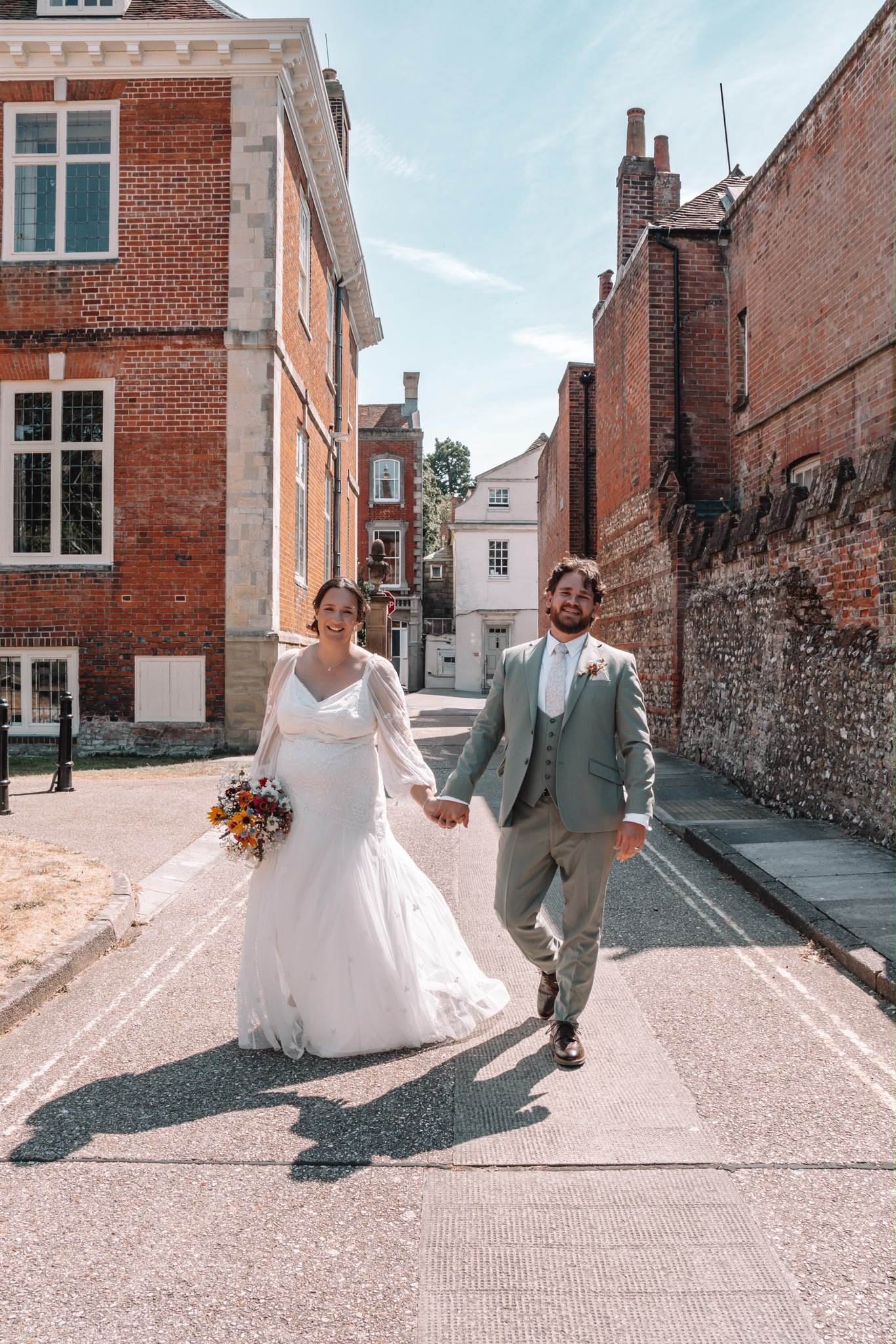 Bride and groom walking hand in hand down a street between historic brick buildings