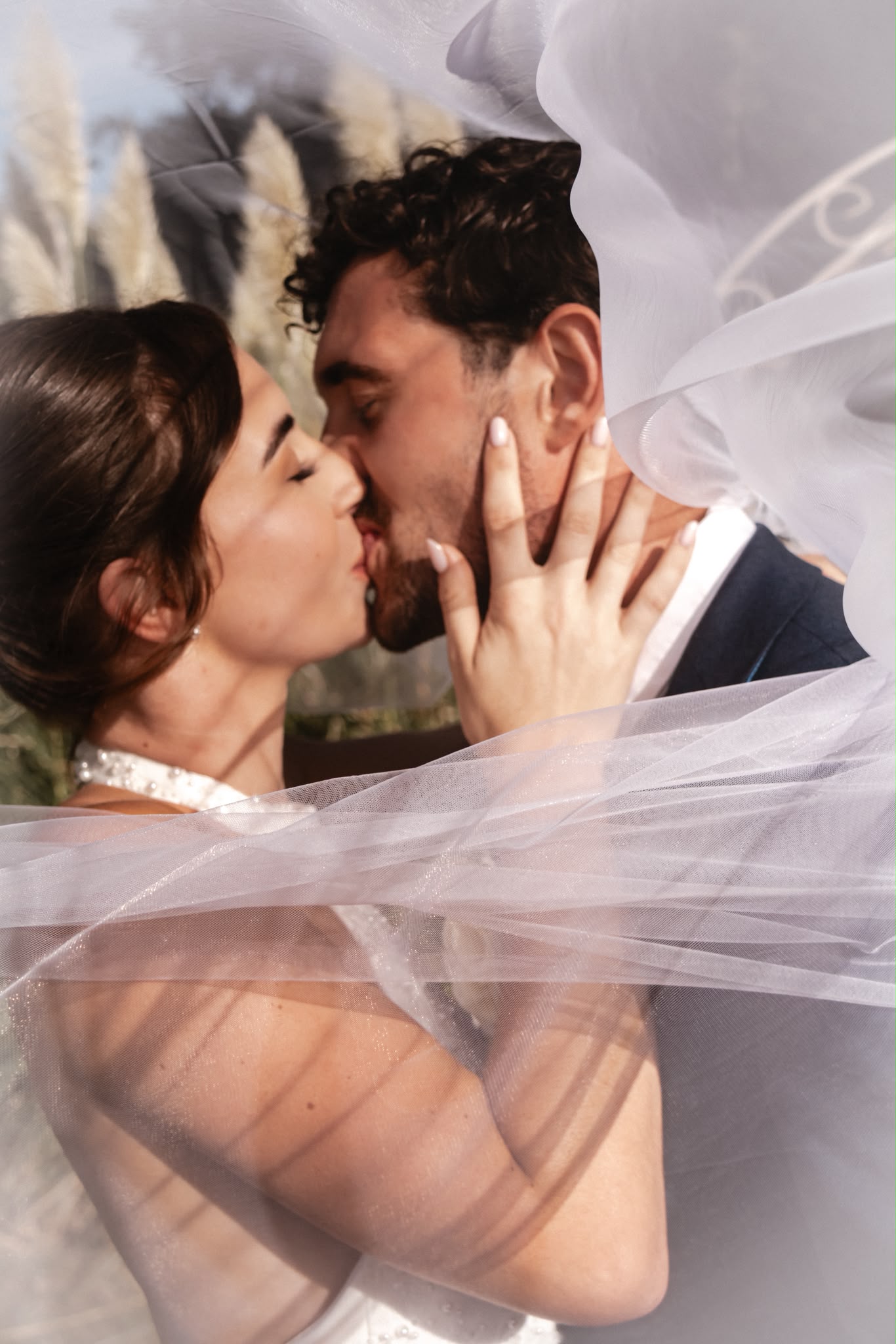 Close-up of a bride and groom sharing a kiss beneath a lace veil at golden hour