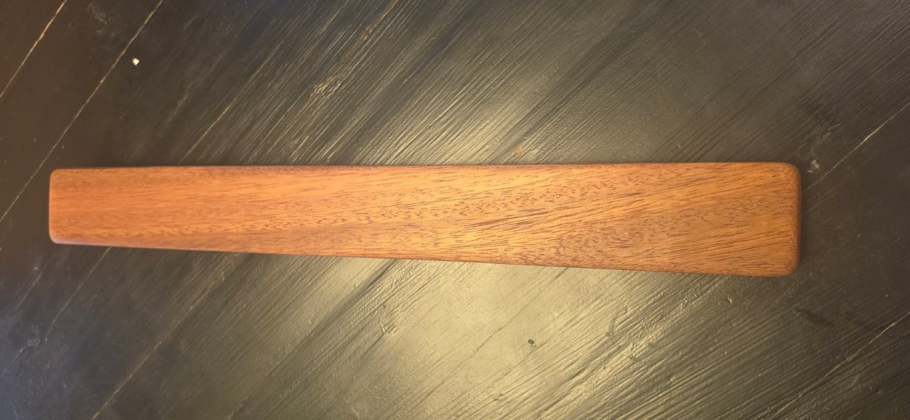 A single elongated wooden component with visible natural grain and rounded corners resting on a dark surface