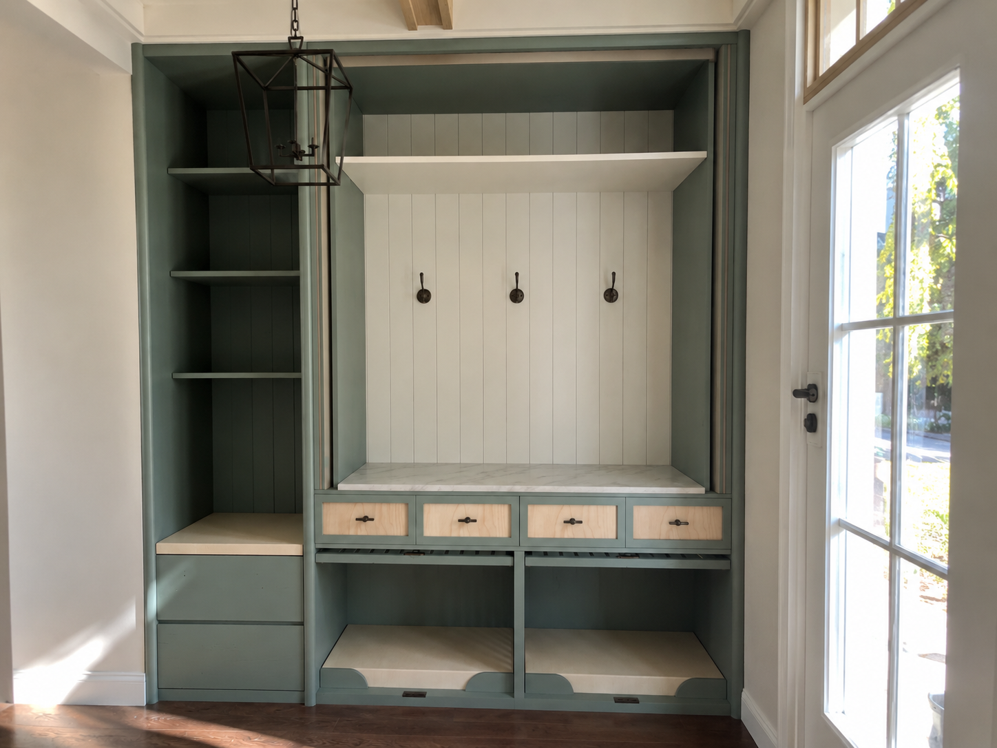 Sage-green entry joinery with hooks, a bench, drawers and two low pet alcoves beneath