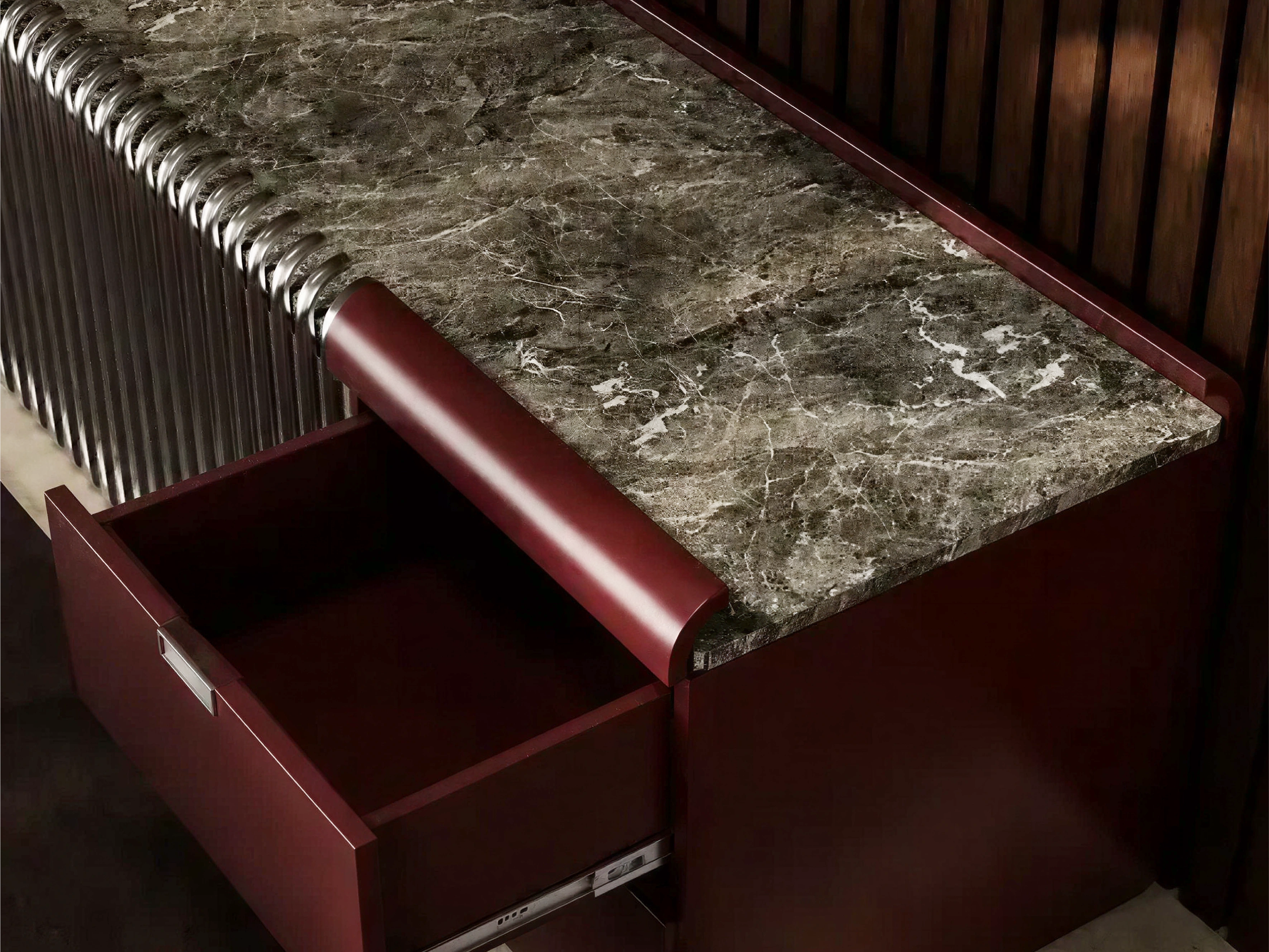 HĀM concept study close-up of a veined stone surface, curved lacquered drawer front and metal bars.