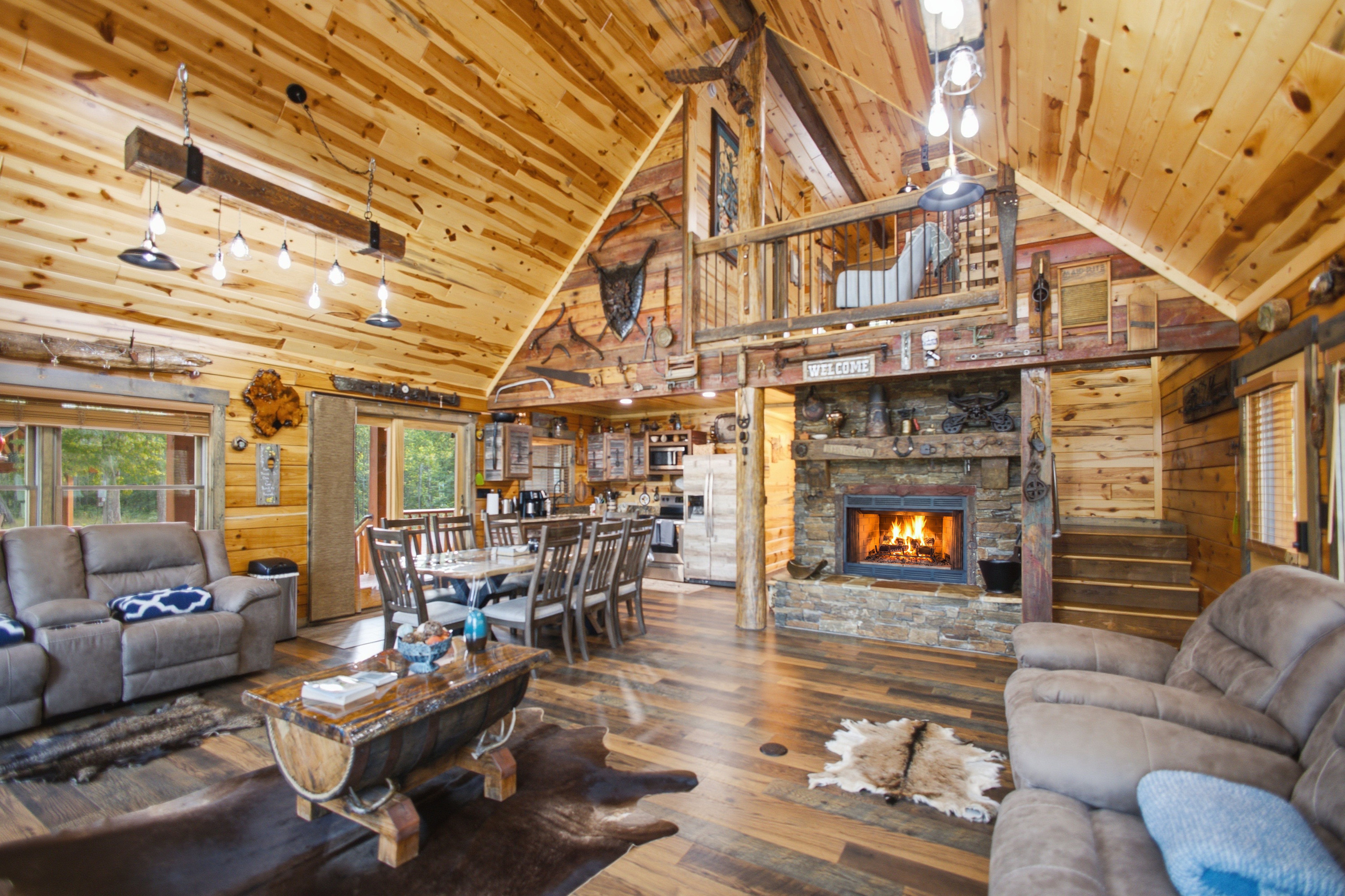 Northwoods cabin living room with vaulted wood ceiling, loft, stone fireplace, and open dining area