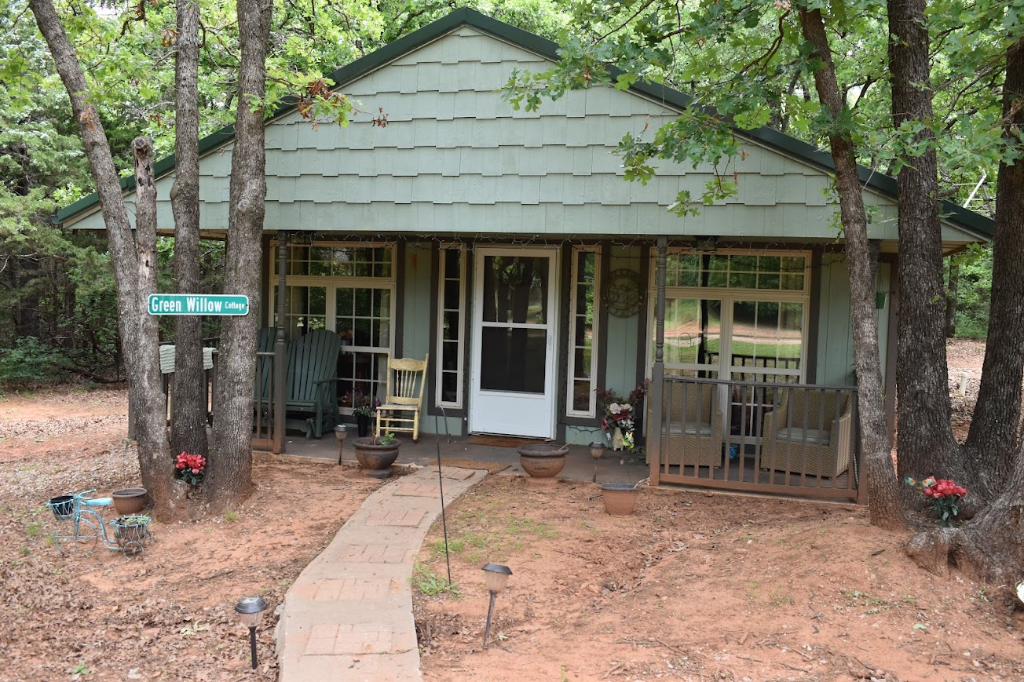 Green Willow cottage exterior with sage green siding nestled among blooming oak trees in Guthrie Oklahoma