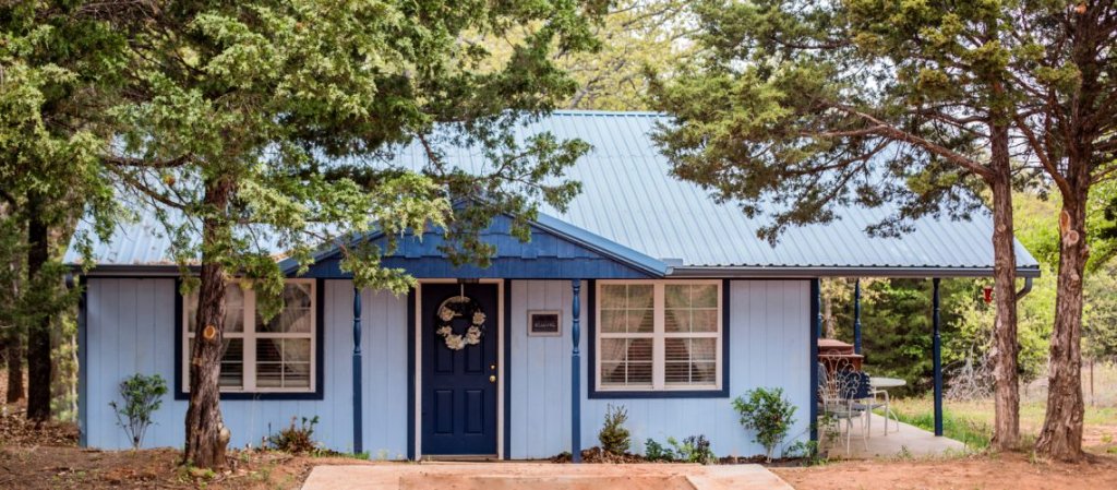 Blue Hideaway cottage exterior with light blue siding nestled among cedar trees in Guthrie Oklahoma