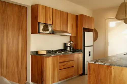 Solid Cherry Wood kitchen — flat-sawn cut, natural warm finish. Full-height upper cabinets with integrated stainless appliances and granite countertops. A warm, functional kitchen built to last decades.
