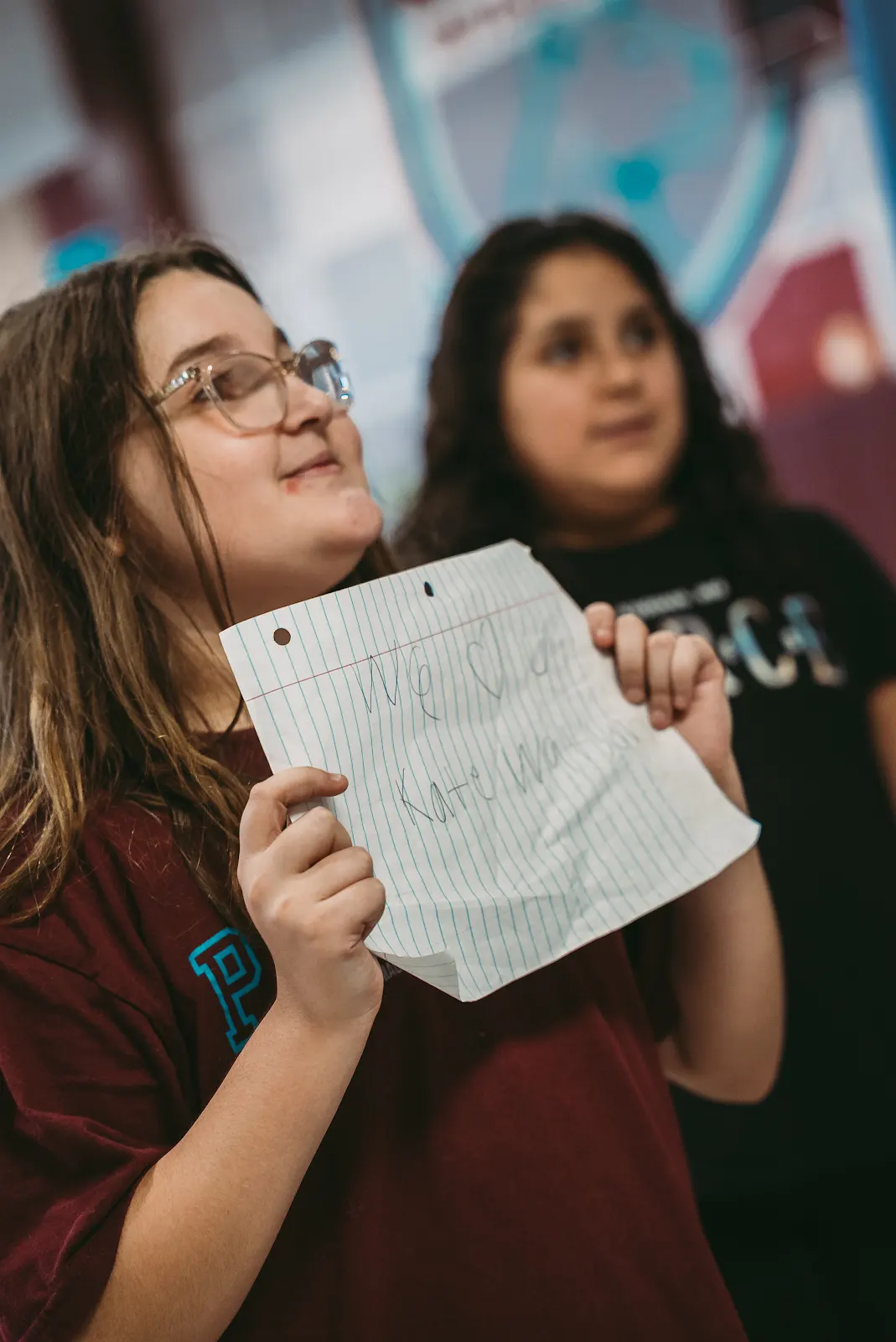 A student holding a handwritten 'We love u Kate Watson' sign