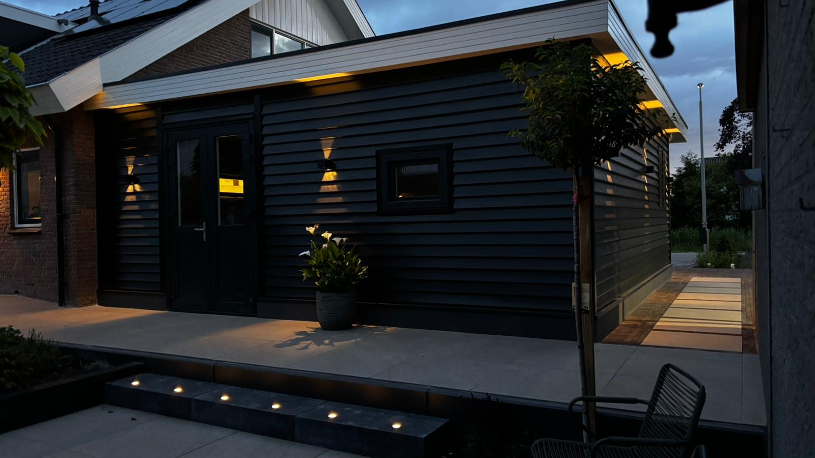 Aanbouw garage en schuur met zwarte houten gevel bij avond — signature case YMD Bouw