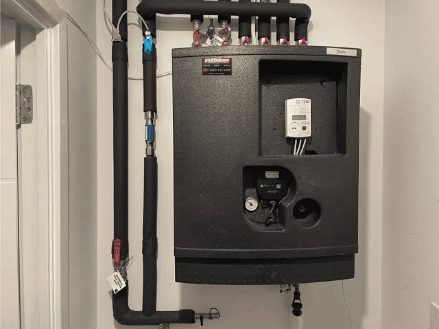 Wall-mounted Danfoss HIU installed in a flat with insulated pipework