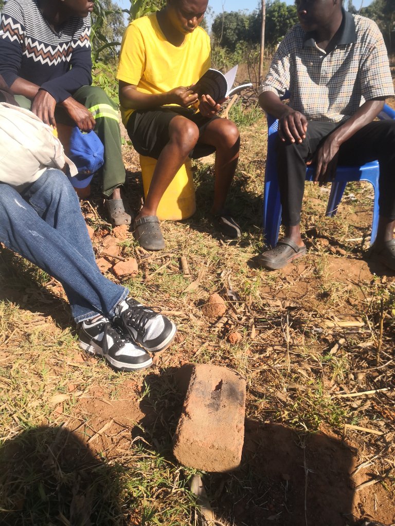 Three community members sitting outdoors reading The Prayer together in Malawi