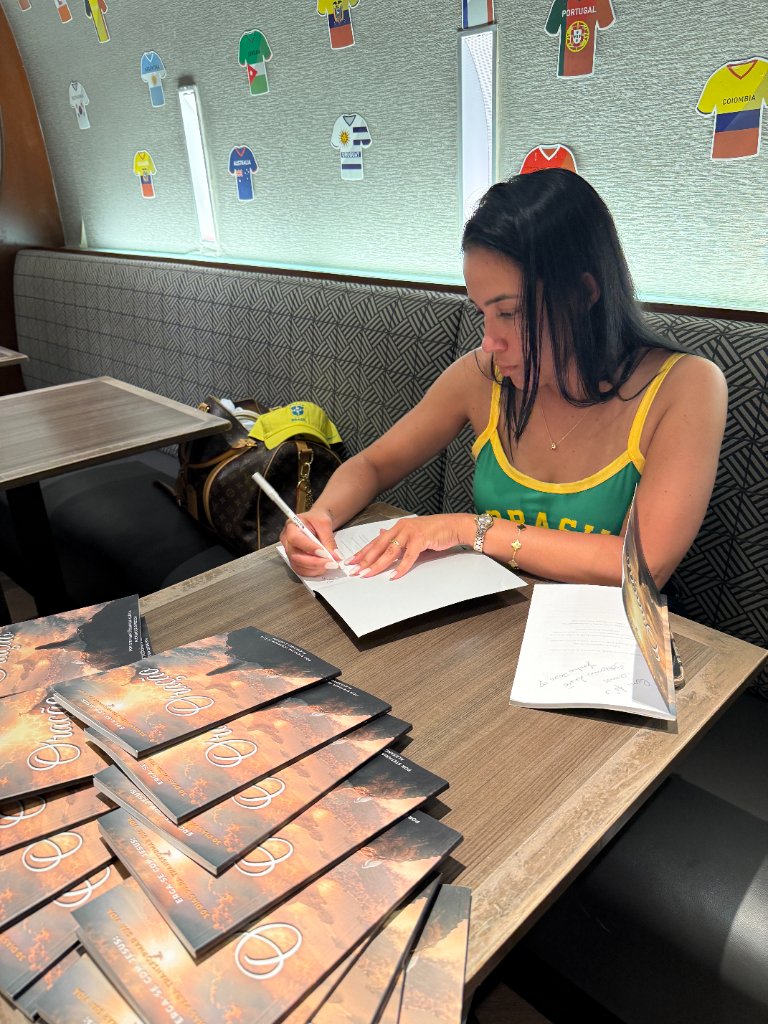 Stefania Leão in a Brazil-themed tank top signing copies of Oração at a table with a stack of books during the FIFA World Cup
