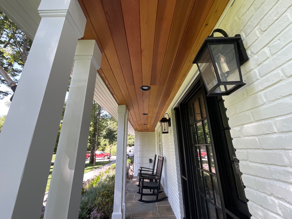 Front entry porch with cedar ceiling, white columns, and black door