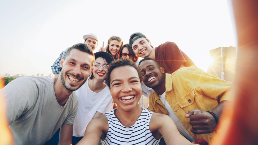 A diverse group of young adults smiling together in an outdoor selfie during golden hour