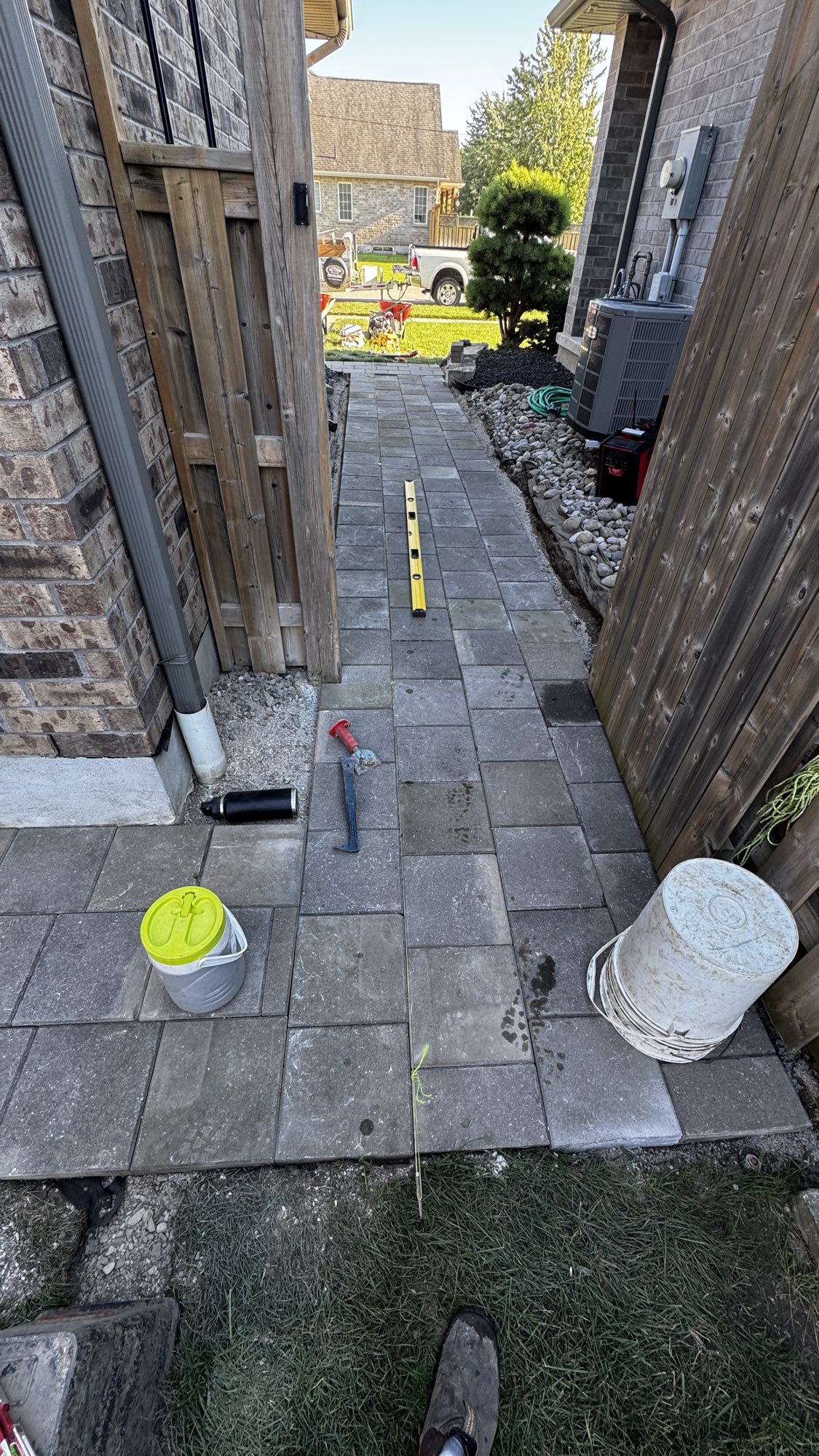 Side yard walkway during — yellow level resting on freshly laid pavers to check grade
