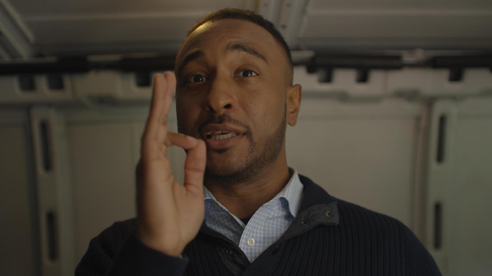 A character making an OK gesture inside the production van, production still from the film Doctored