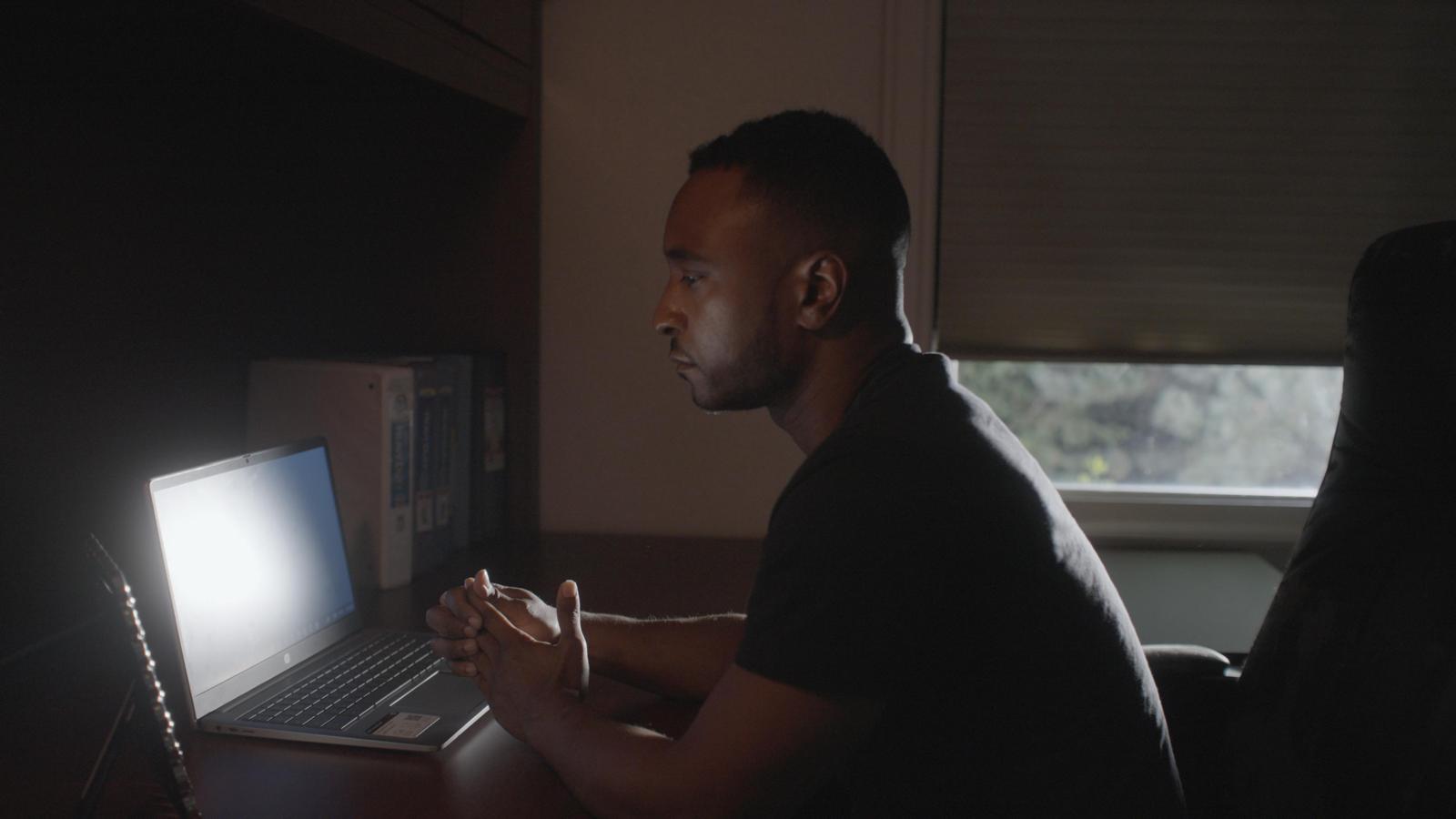 Investigator at a laptop in a dimly lit office, production still from the film Doctored