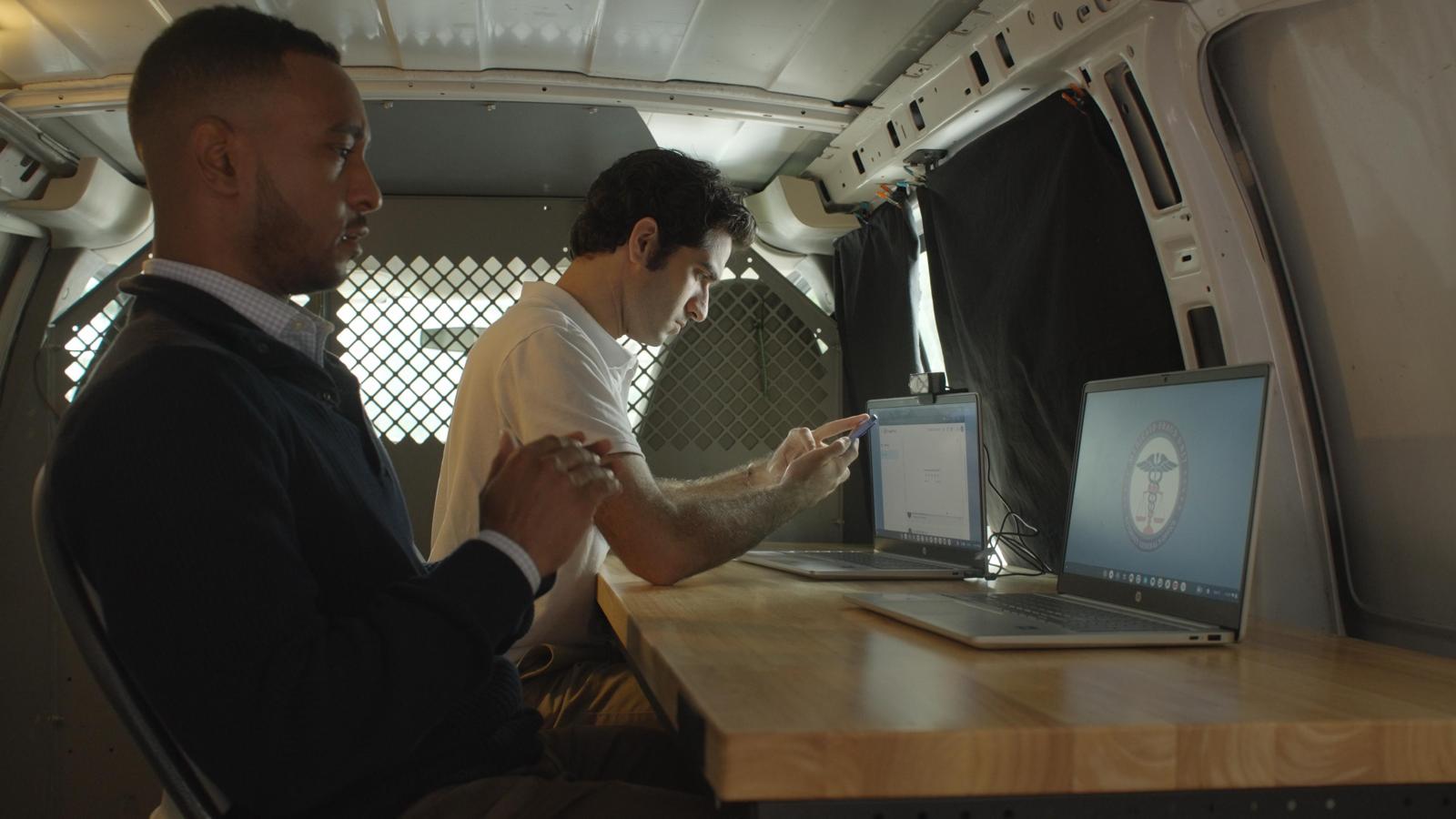 Two investigators at a laptop inside the production van, production still from the film Doctored
