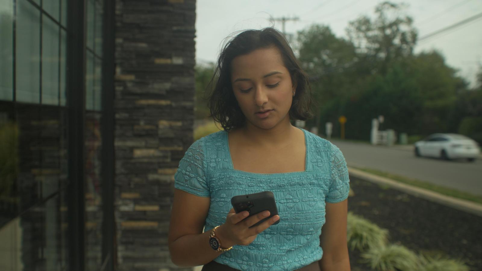 Actor in a teal lace top looking at a smartphone on the set of the film Doctored