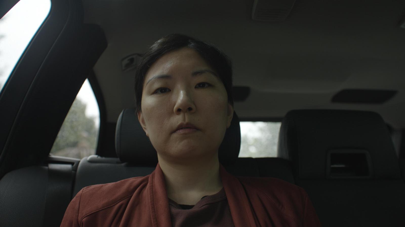 Close-up film still of a woman seated in the back seat of a car from the film Doctored