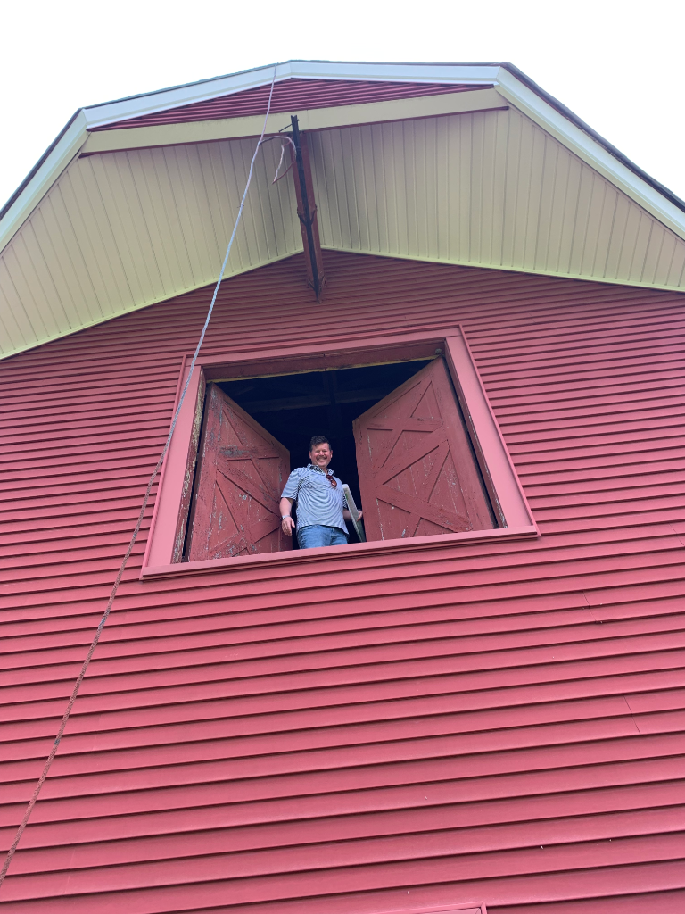Reviewer standing in the barn loft window opening with plans