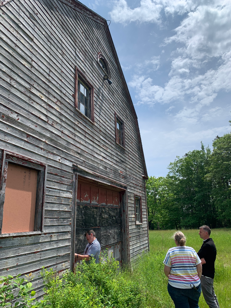 Weathered grey barn with reviewers inspecting the structure