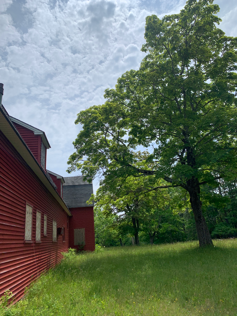 Red barn exterior with boarded windows, viewed from the field