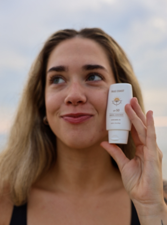 Woman holding True Coast sunscreen tube at sunset
