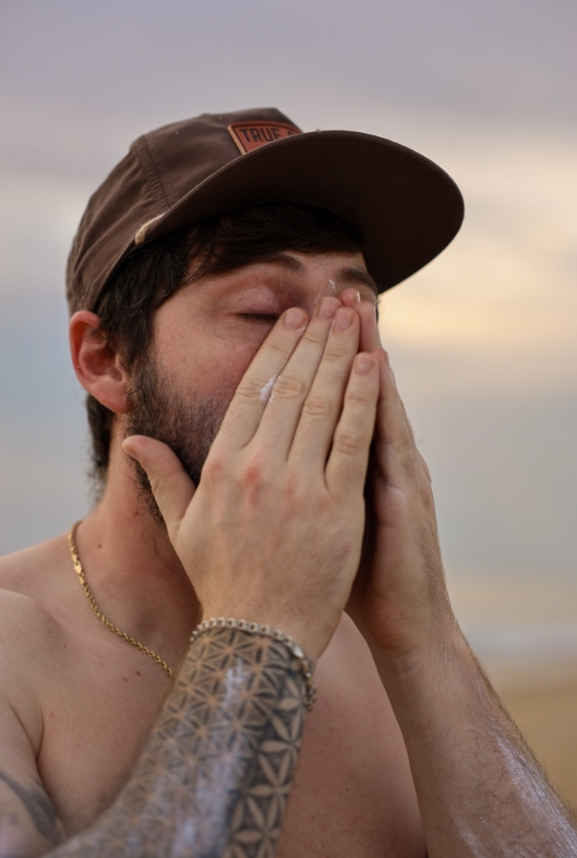 Applying sunscreen to face behind surfboard