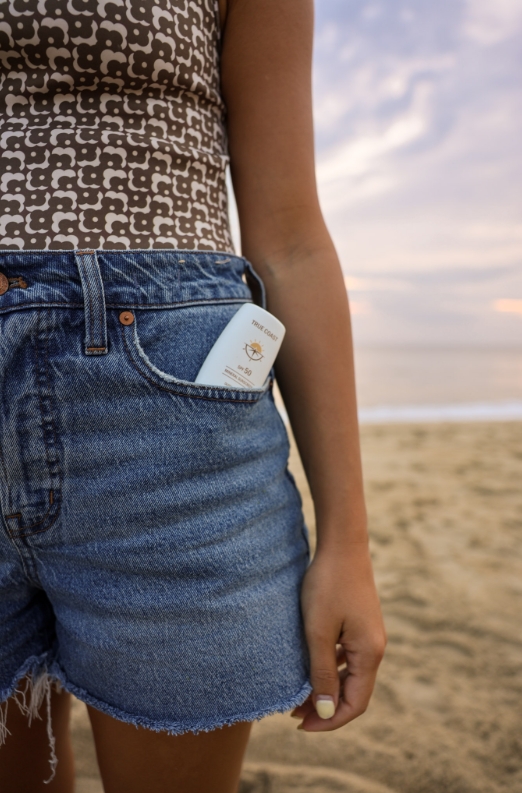 True Coast SPF 50 bottle tucked in denim shorts pocket