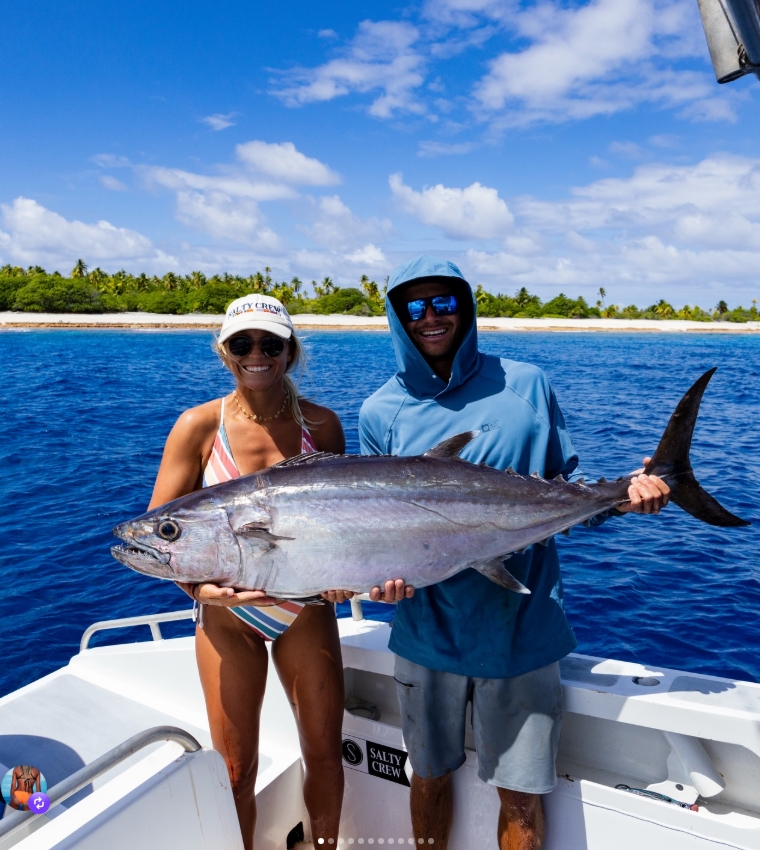 Couple holding a large tuna on a boat in blue offshore waters