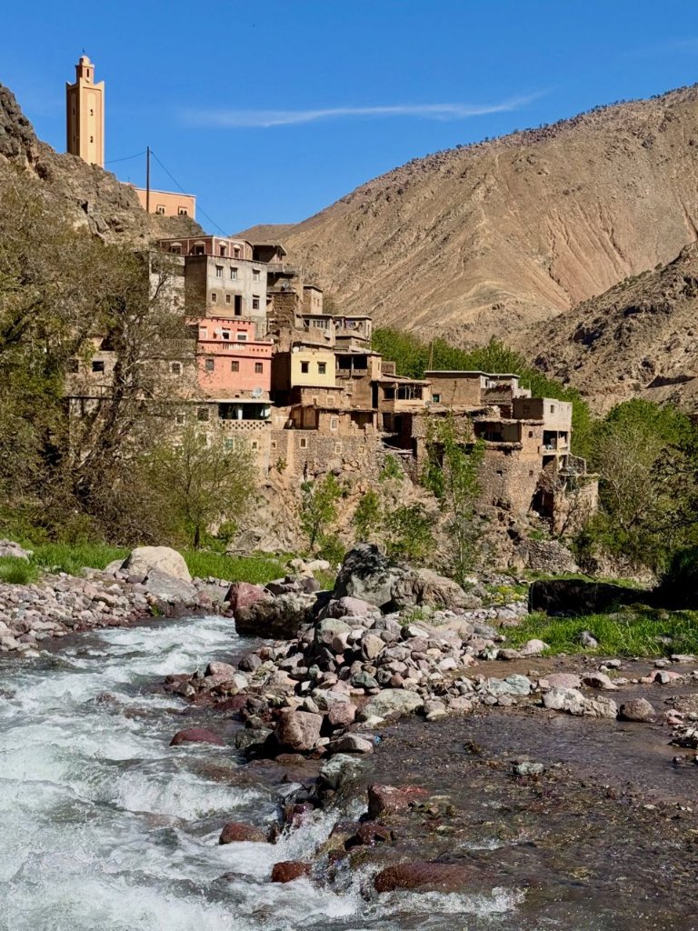 A mountain stream flowing through Imlil village with traditional stone buildings and a mosque minaret