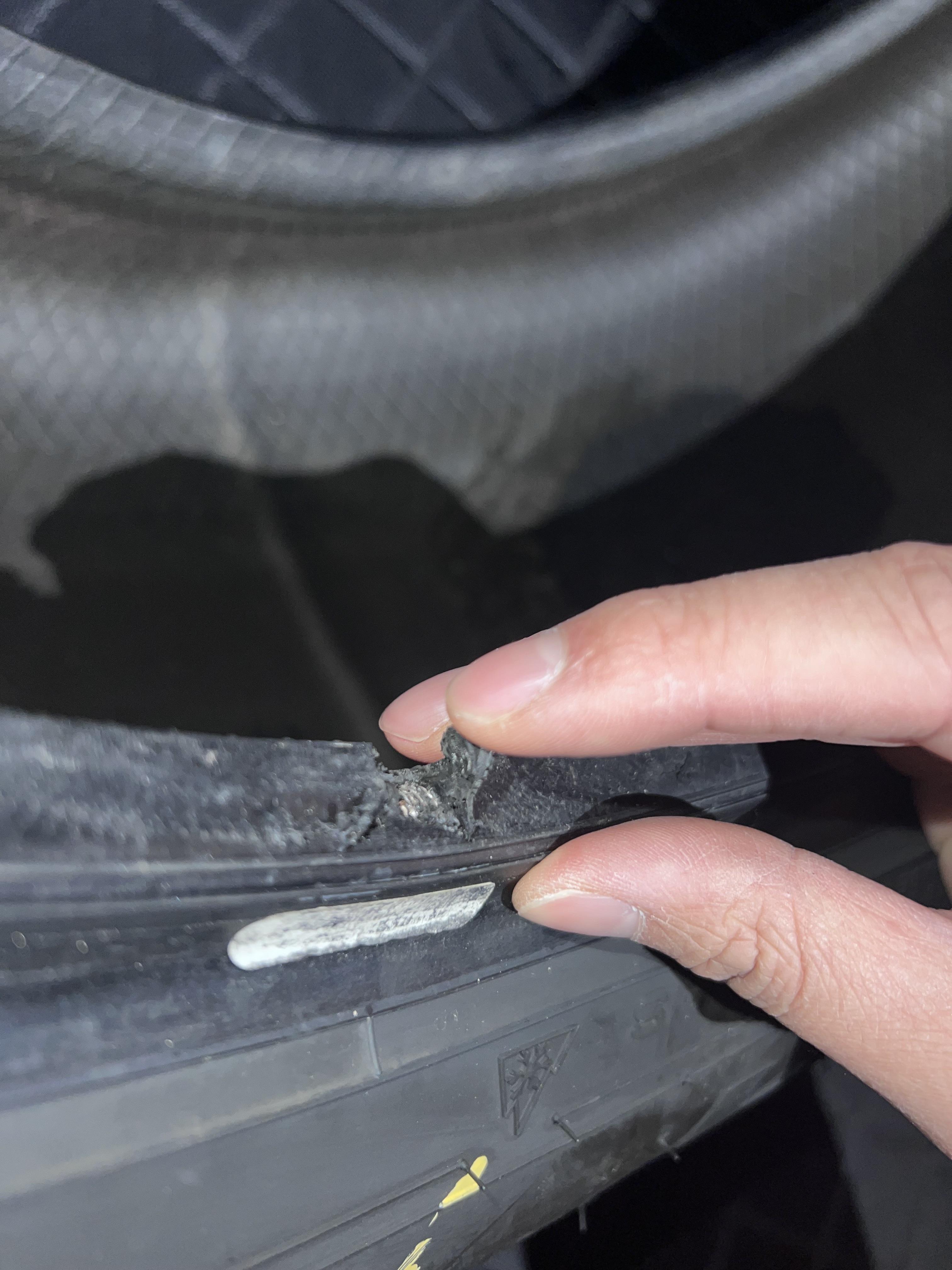 A hand pulling back torn rubber at a tyre bead to reveal the underlying steel wire and casing cords.