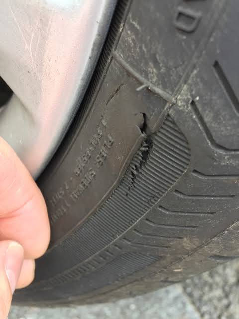 Close-up of a jagged tear in a tyre sidewall near the shoulder, exposing fibrous casing material beneath the rubber.
