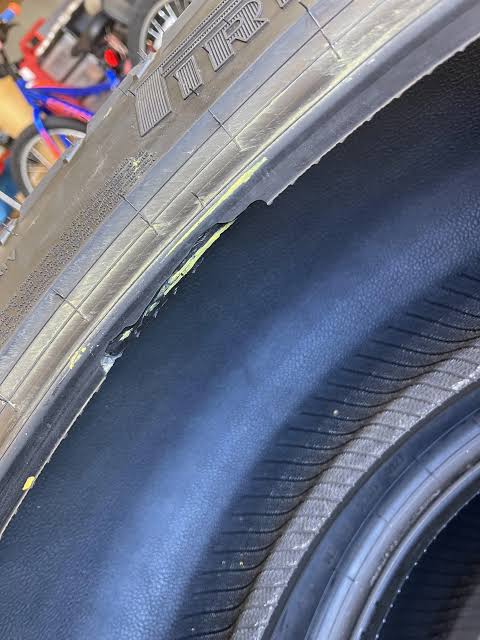 Close-up of a jagged tear in a tyre bead, exposing dark fibrous structural material beneath the rubber.