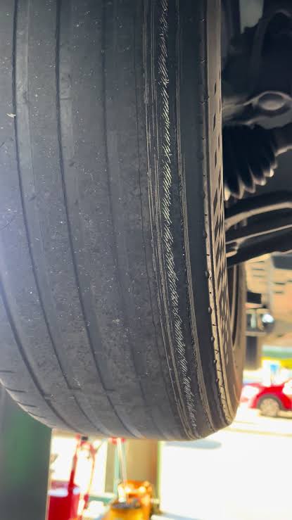Close-up of a tyre tread shoulder showing a worn, abraded groove with frayed rubber and exposed belt material.