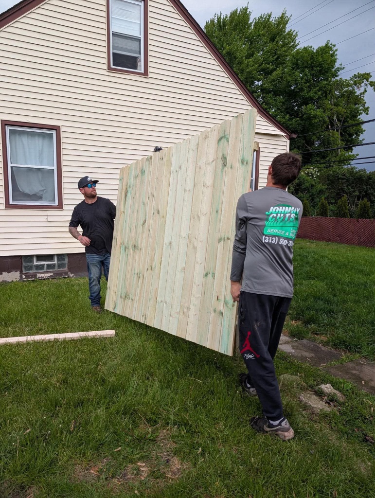 Two workers carrying a heavy wooden fence panel