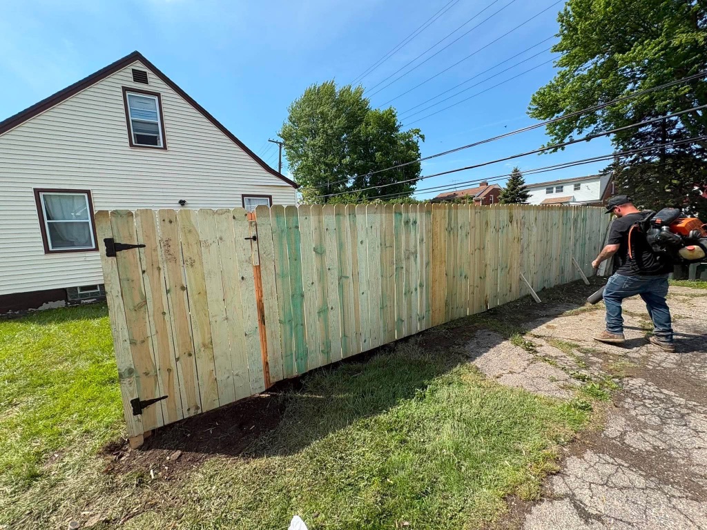 Worker blowing debris near newly installed wooden fence