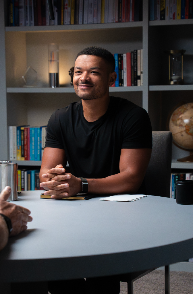 Man seated at a round table in a bookshelf-lined studio