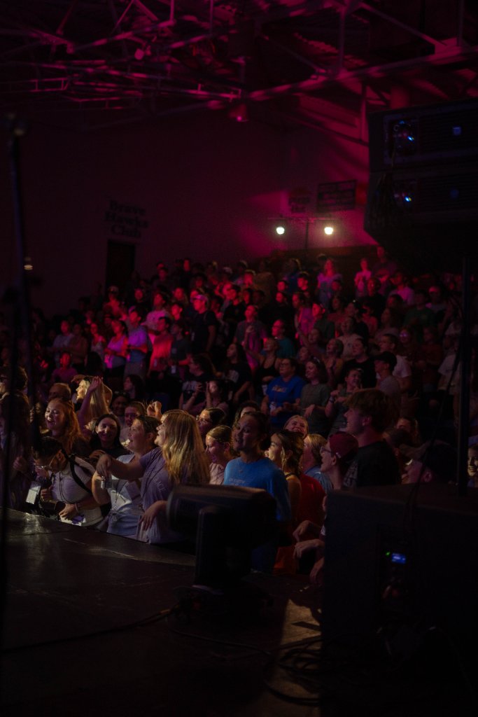 Students in bleachers lit by warm stage lighting at camp